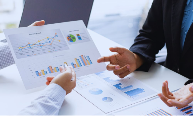 Small business growth consultant meeting with a client at a desk, reviewing printed business charts and performance data to discuss strategies for company growth.